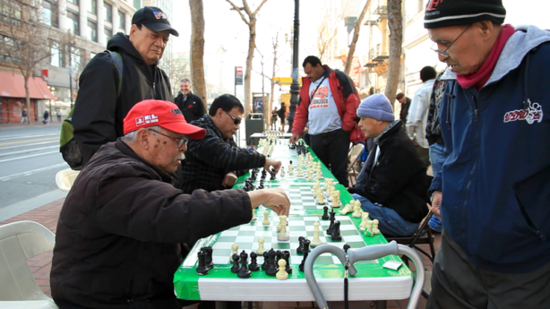 a group of people playing chess on a really long green chess table