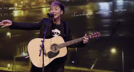 denise ho holding her guitar behind a microphone.