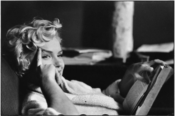 image of marilyn monroe sitting with her finger on her eyebrow holding her head, while holding a book in front of her lap.