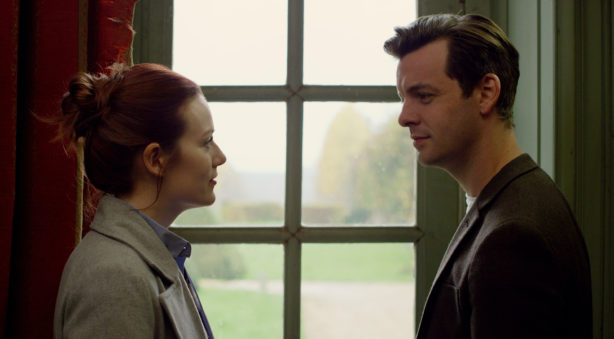 A man and a woman standing by a window staring at each other