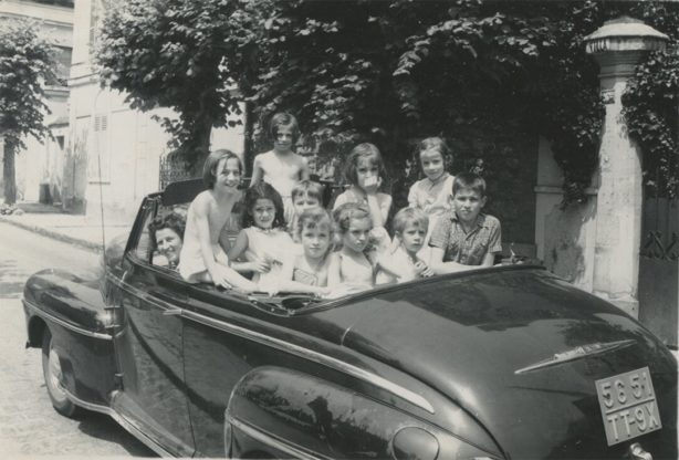 A black and white photo of a open-topped car full of children.