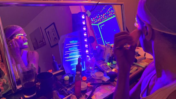 A person applies blacklight-responsive make-up while sitting at a mirror.