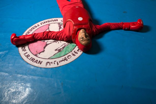 Woman laying down on martial arts platform with arm spread in full gear.