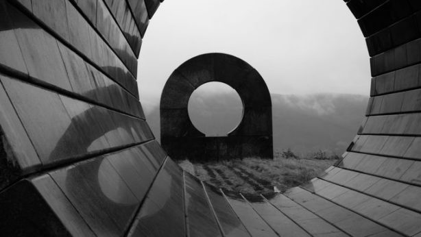A ribbed, spiraling stone sculpture frames another structure in the distance