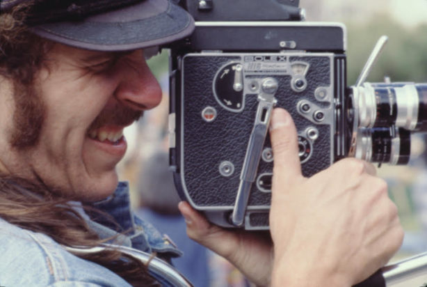 A man with a hat looks through the eyepiece of his film camera.