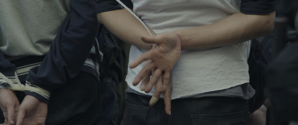 A close-up of two people, each with their hands zip-tied behind their backs