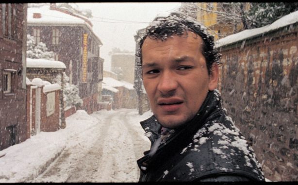 A man facing our direction but looking beyond us, with a snowy street in the background
