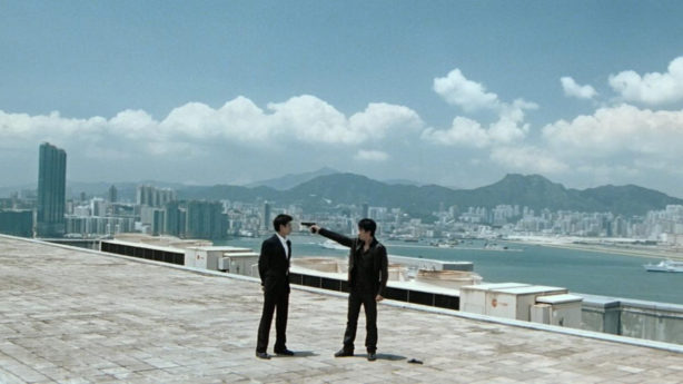 2 men on a building top, one with a gun to the head of the other, and Hong Kong in the backgroumd.