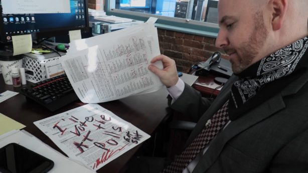 A election official examines a mail-in ballot which has been scrawled over with the words "I'll at the polls. EAT SHIT"word