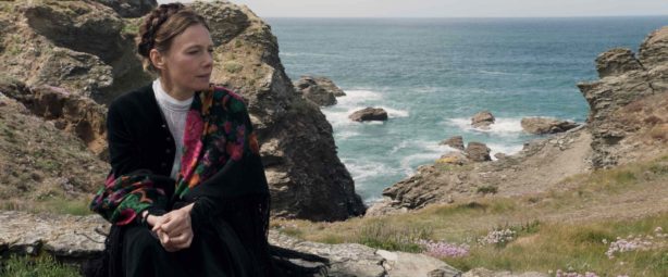 A woman in a shawl looks to her left with the shoreline of Belle Île in the background