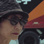 A partial profile of a mysterious woman in sunglasses and a hat.